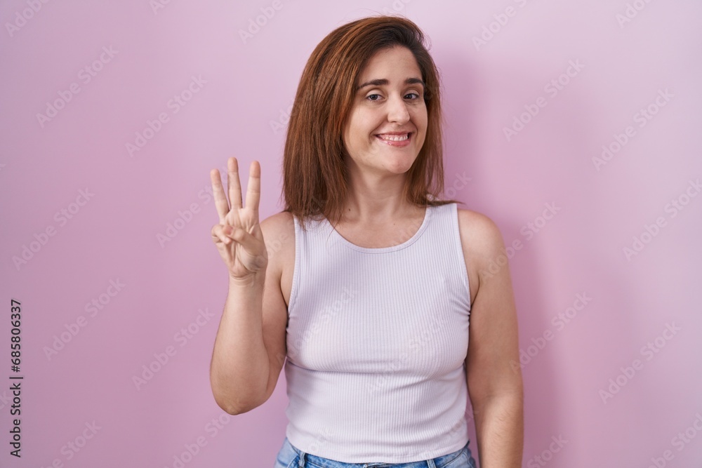 Brunette woman standing over pink background showing and pointing up with fingers number three while smiling confident and happy. Brunette woman standing over pink background showing and pointing up with fingers number three while smiling confident and happy.