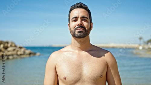 Young hispanic man tourist standing shirtless at the beach