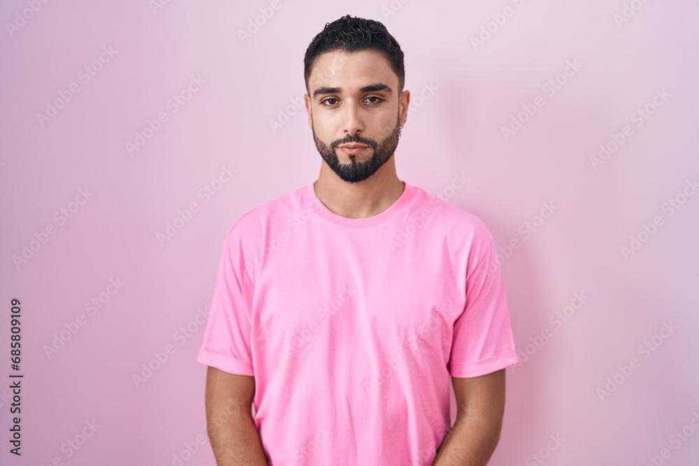 Hispanic young man standing over pink background relaxed with serious expression on face. simple and natural looking at the camera. Hispanic young man standing over pink background relaxed with serious expression on face. simple and natural looking at the camera.