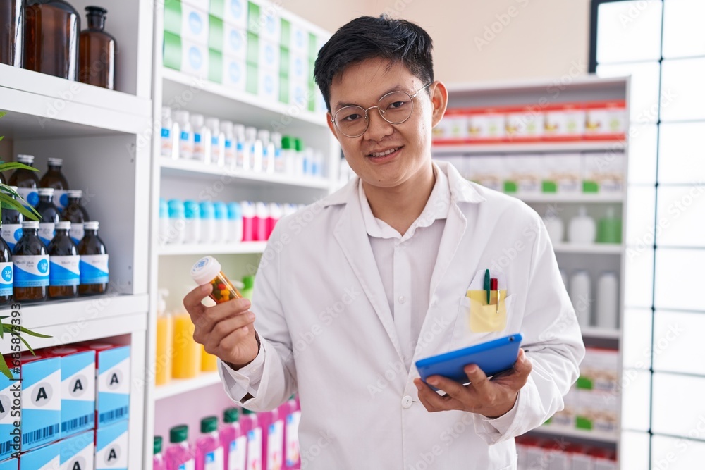 Young chinese man pharmacist using touchpad holding pills bottle at pharmacy