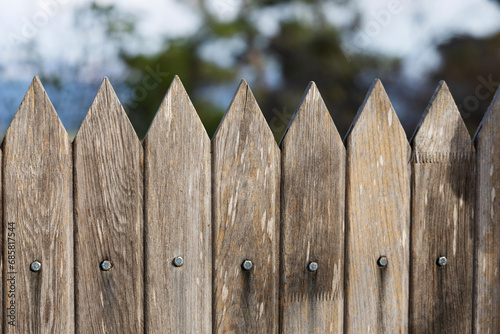Wooden picket fence close-up against the background of the sky, trees and sea.