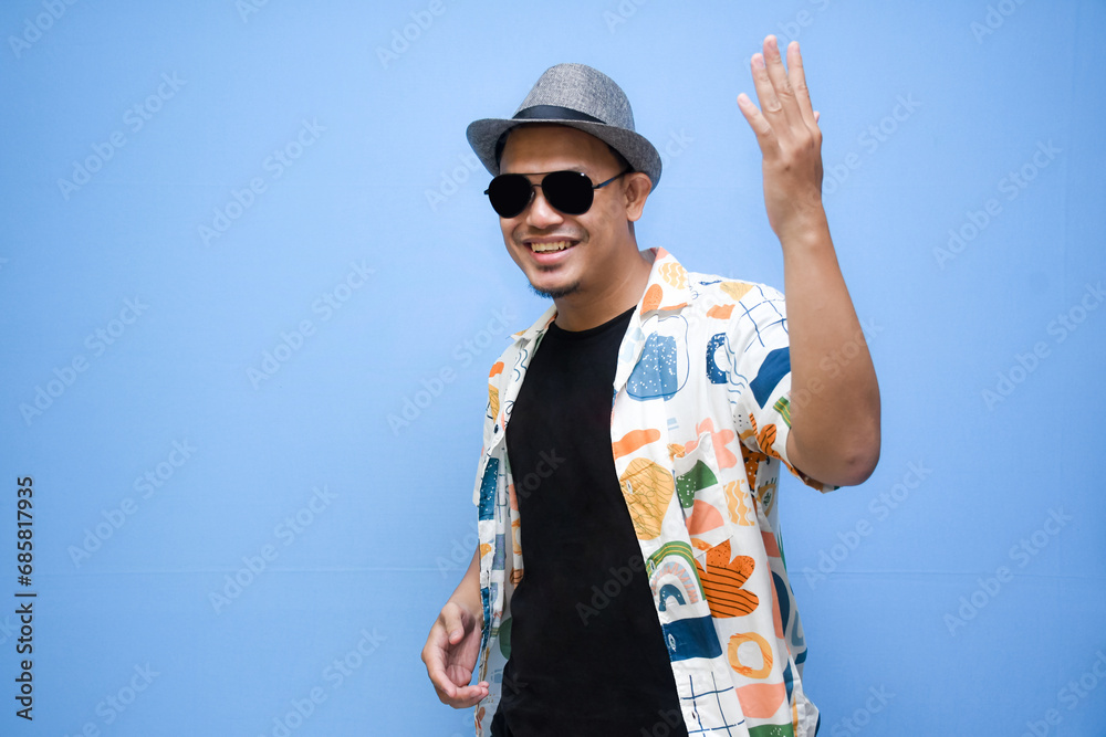 Fototapeta premium asian man wearing beach shirt pointing a finger to vacation discount offer. Isolated on blue background. Vacation concept