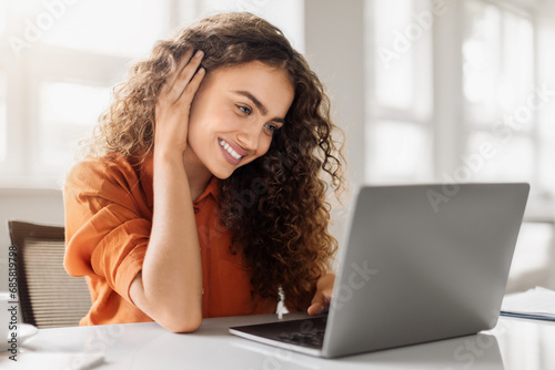 Smiling curly woman with laptop in office photo