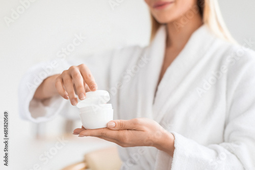 Fototapeta Naklejka Na Ścianę i Meble -  lady holding and opening cosmetic jar with moisturizer cream indoor