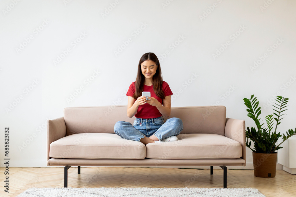 Smiling Young Asian Woman With Smartphone Relaxing On Couch At Home Smiling Young Asian Woman With Smartphone Relaxing On Couch At Home