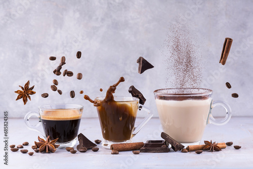 lively composition with espresso, latte and cappuccino in transparent glass cups among floating aromatic spices, chocolate pieces and coffee beans photo