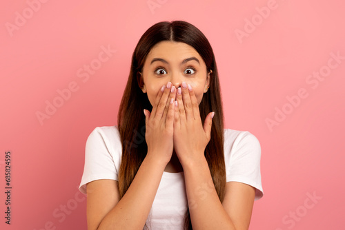 Surprised teen girl covering mouth with hands and looking at camera
