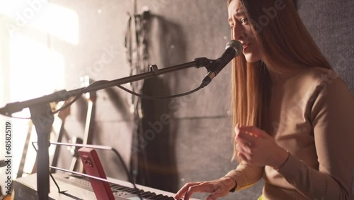 Beautiful musician woman sings and plays synthesizer at rehearsal for performance with her music band in recording studio. Voice training and teaching by professional artist singer. photo