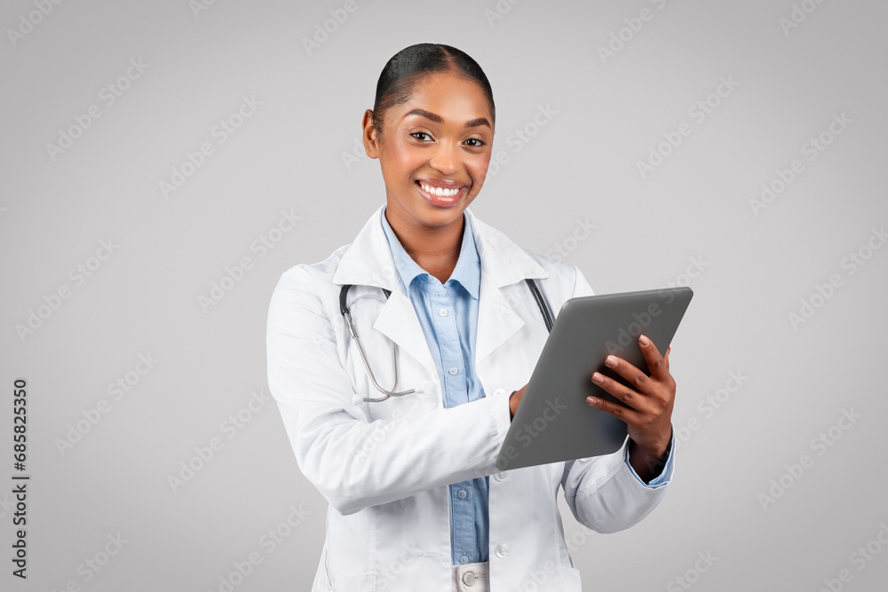 Positive young black woman doctor in white coat, chatting at tablet, typing Positive young black woman doctor in white coat, chatting at tablet, typing