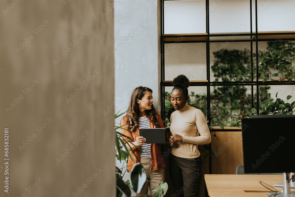 Two young business women with digital tablet standing in the modern office Two young business women with digital tablet standing in the modern office