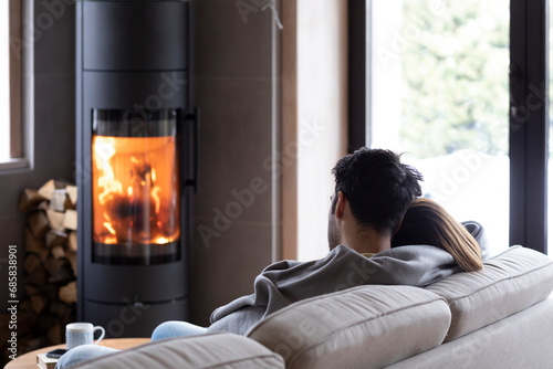 Back view on cute lovers sitting on the couch close to fireplace. Young couple spending time together in the cozy home photo