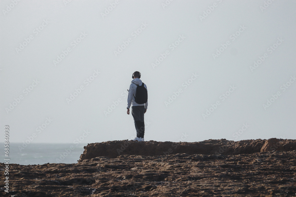 Obraz premium Young man standing on the top of a rock in a beach