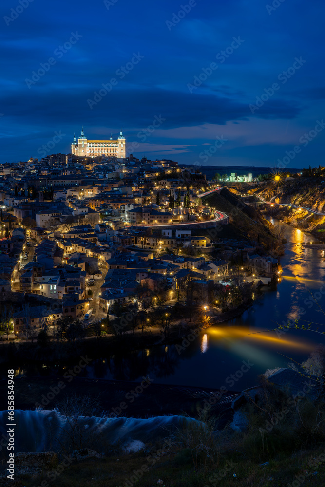 Vertical view of the historic center of Toledo, Spain, at night with the Alcázar (now the army museum) illuminated and the Tagus River surrounding the city. UNESCO World Heritage Site