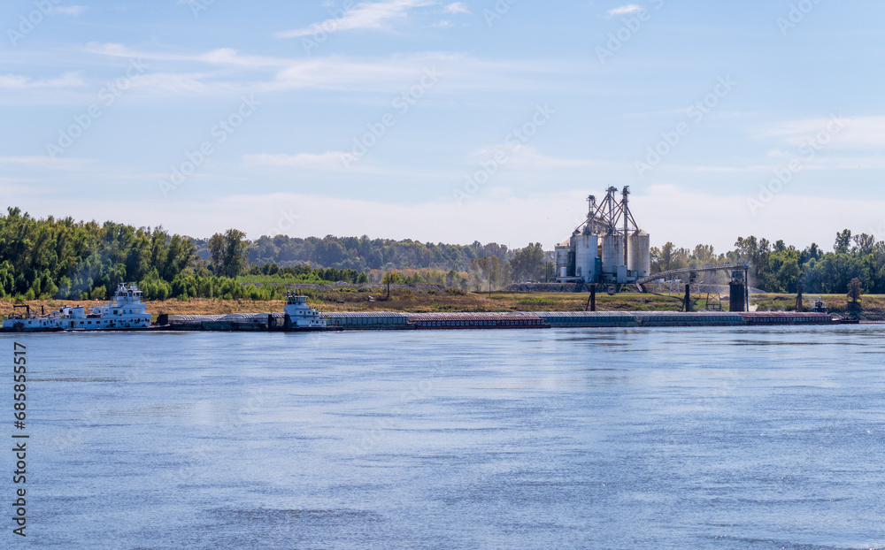 Fototapeta premium Tugboat pushing freight barges past grain loading dock in farming country in Kentucky