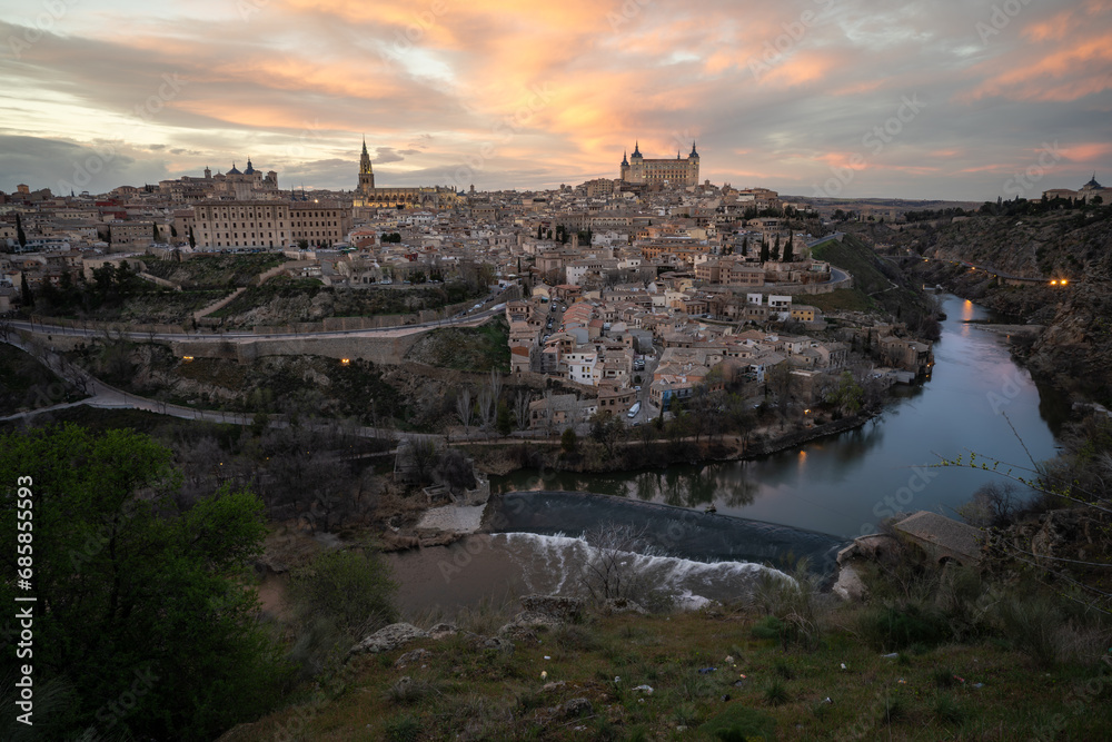 Historic city of Toledo with the a weir of Tagus River in foreground from a viewpoint of the city at sunset with reddish sky. UNESCO World Heritage Site