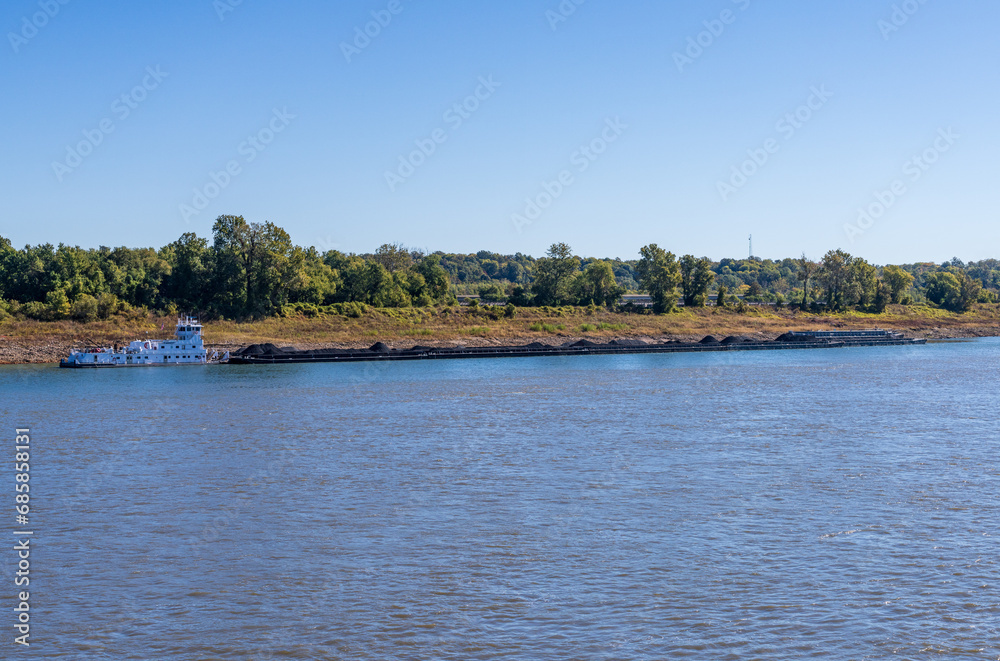 Large tug boat pushing rows of barges with coal products down the Mississippi river south of Cairo in Illinois