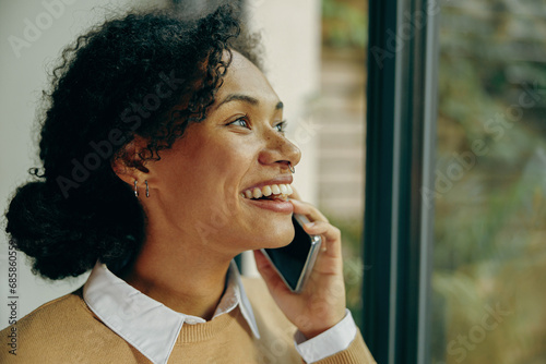 Smiling female freelancer talking on mobile phone with client while work from home office