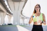 Pretty brunette young woman opening bottle with water during break of training standing under overpass wearing. Sport clothes. Sporty Spanish girl in yellow bra confidently looking aside. Healthcare.