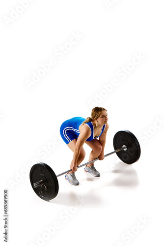 Top view. Full-length of young athlete, girl training, lifting heavy weights, barbell against white background. Concept of sport, strength, gym, healthy lifestyle, power and endurance, weightlifting.