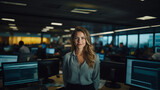 confident woman in large office with computer monitors, surrounded by people working collaboratively, exuding positivity and determination
