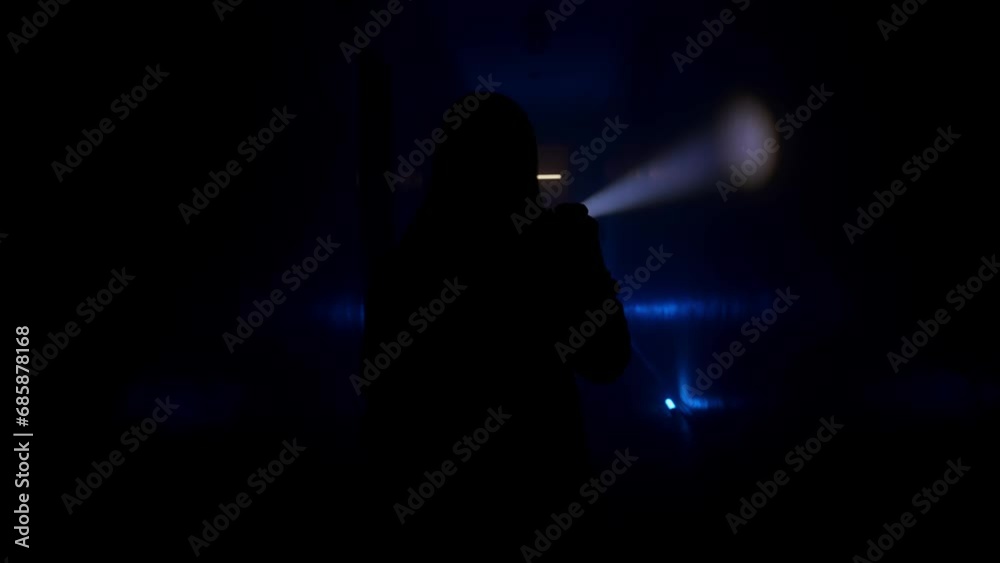 Woman with a flashlight walks along a dark corridor. Back view Woman with a flashlight walks along a dark corridor. Back view