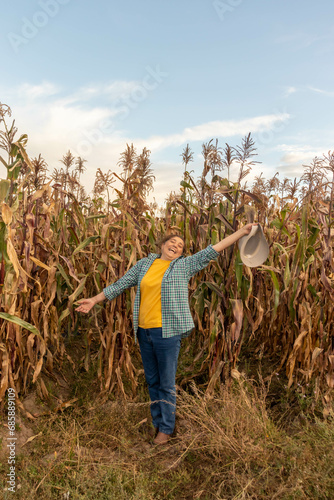 Mujer adulta en sus 50 años frente a una plantación de maíz celebrando con los brazos extendidos y mirando hacia el cielo como simbolo de libertar y alegría photo