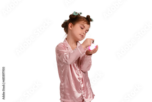 Cute little girl with curlers in pink silk pajamas on a white background is wearing perfume