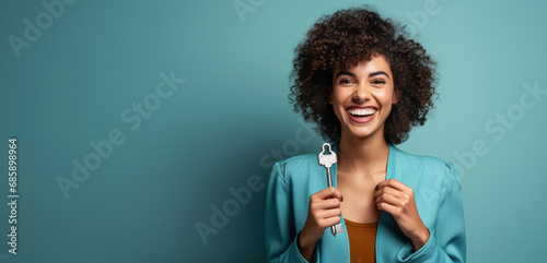 A joyful woman with a key. A cheerful young woman with curly hair holds a key isolated on a blue background, a banner.