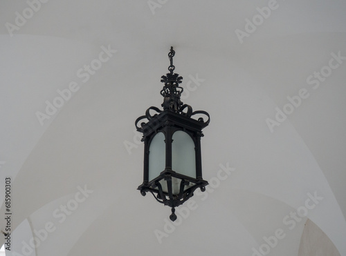Vintage iron lantern hanging on concrete wall in evening time. Old lamp illuminating urban street.