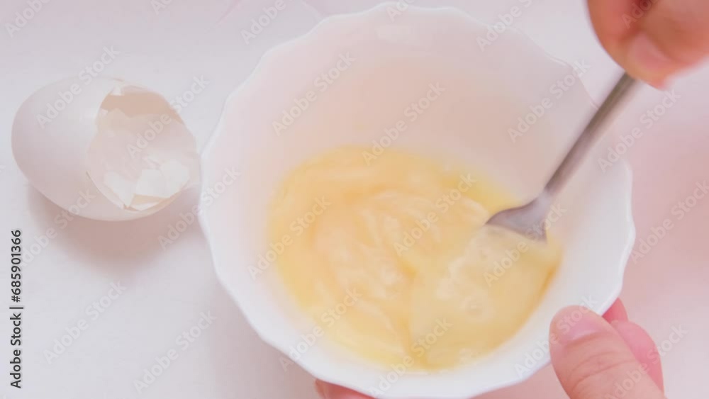 female hand whisks raw chicken egg with fork in white plate, cooking and household skills, specifics of nutrition in sports and training, culinary articles and recipes using eggs female hand whisks raw chicken egg with fork in white plate, cooking and household skills, specifics of nutrition in sports and training, culinary articles and recipes using eggs