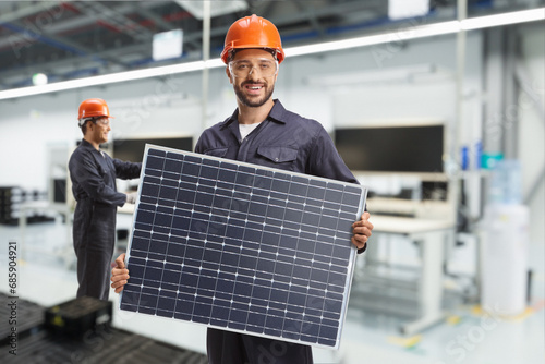 Worker in a uniform holding a solar panel in a factory photo