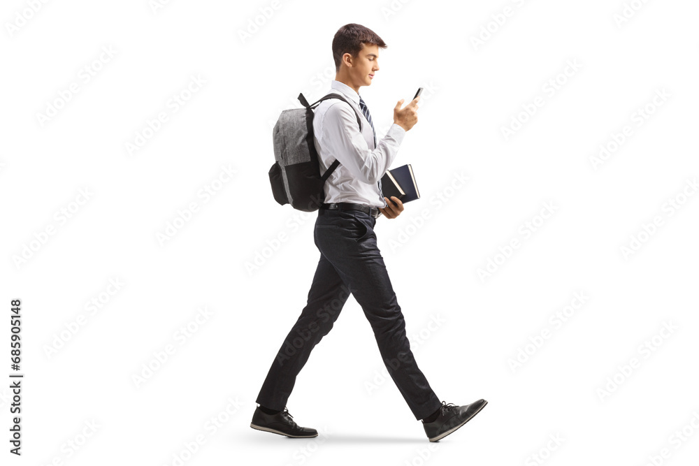 Full length profile shot of a male student in a college uniform walking with a smartphone Full length profile shot of a male student in a college uniform walking with a smartphone