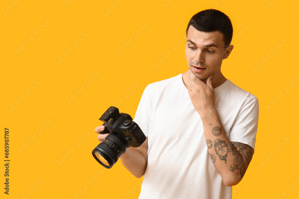 Thoughtful male photographer with modern camera on yellow background Thoughtful male photographer with modern camera on yellow background