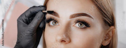 Young woman face during professional eyebrow mapping procedure before permanent makeup and lamination. Artist does long-lasting styling of the eyebrows with hair coloring. Panorama with copy space.