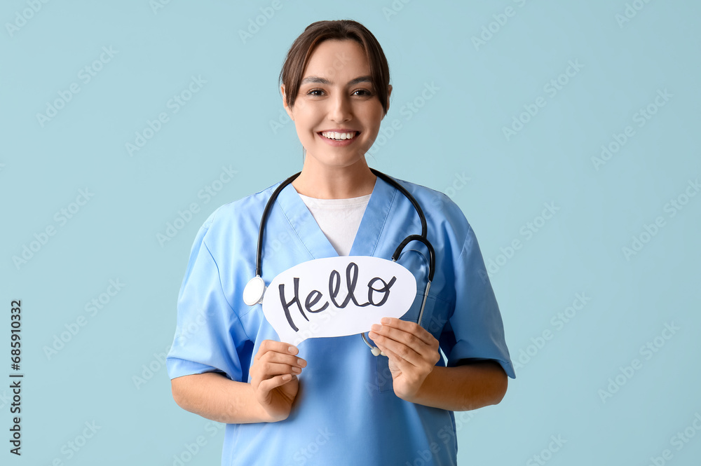 Beautiful female doctor holding paper speech bubble with word HELLO on blue background Beautiful female doctor holding paper speech bubble with word HELLO on blue background