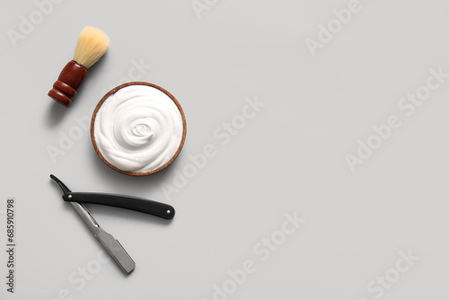 Brush with bowl of shaving foam and razor on grey background