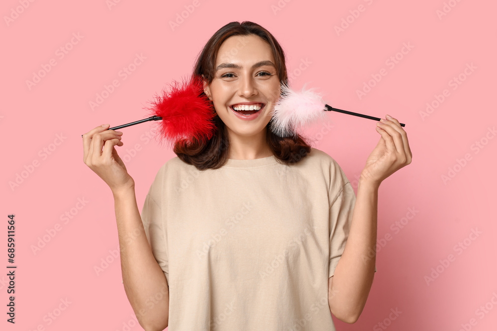 Obraz premium Happy young woman with feather sticks on pink background