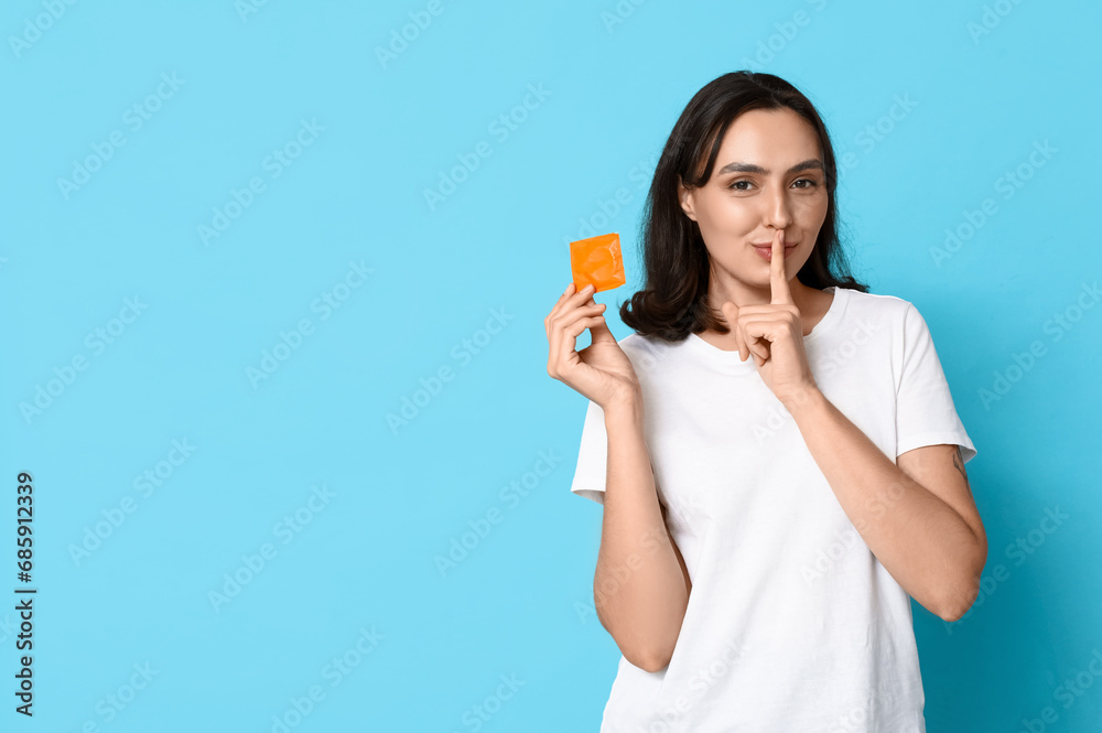Young woman with condom showing silence gesture on blue background. Safe sex concept Young woman with condom showing silence gesture on blue background. Safe sex concept