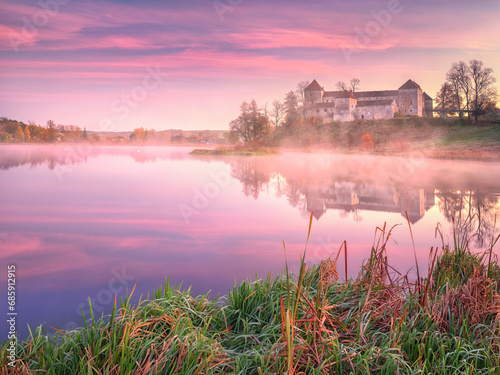 pink morning colours above lake and old castle with reflections in water