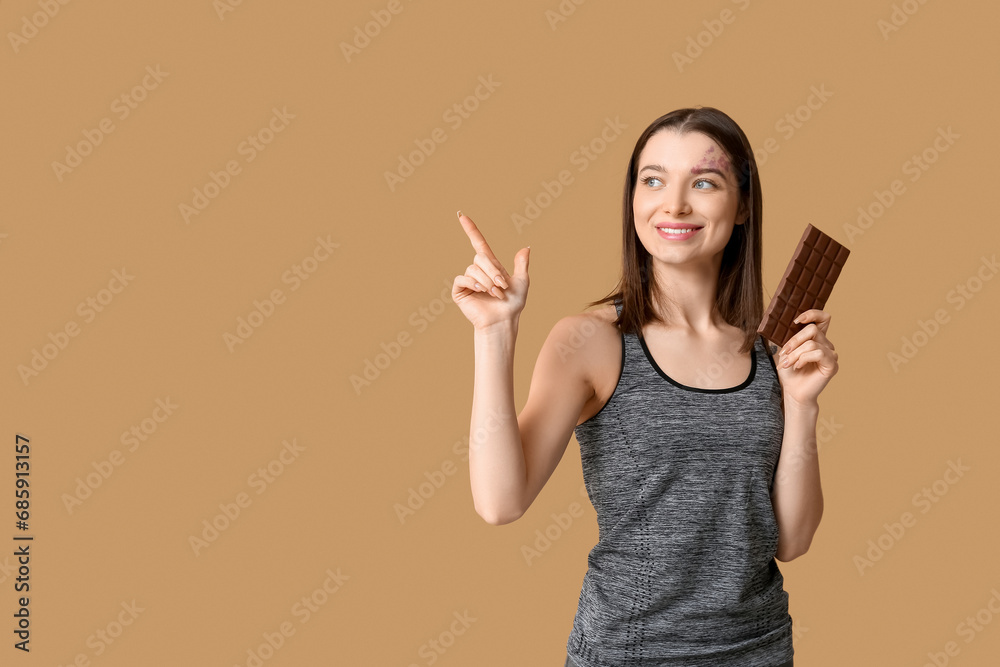 Young woman holding chocolate bar and pointing at something on brown background Young woman holding chocolate bar and pointing at something on brown background