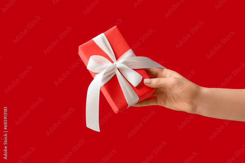 Female hand with Christmas gift box on red background Female hand with Christmas gift box on red background