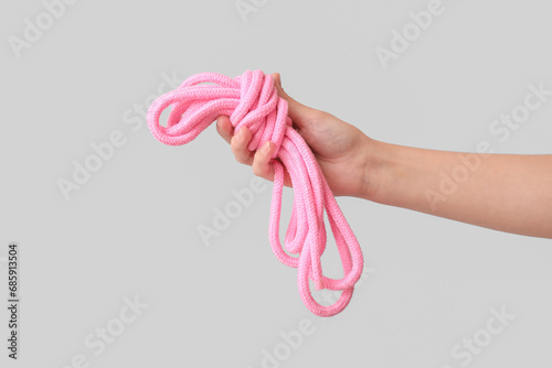 Female hand with pink rope from sex shop on grey background, closeup