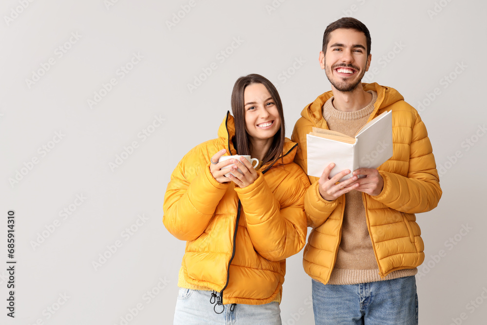 Loving couple in winter clothes with cup of tea and book on light background Loving couple in winter clothes with cup of tea and book on light background