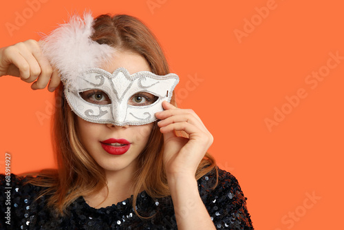 Beautiful young woman in white carnival mask on orange background