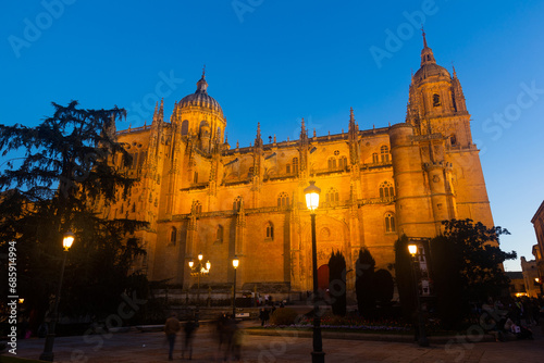 Illuminated north facade of impressive gothic building of New Cathedral of Salamanca with tall bell tower and baroque dome as seen from Plaza de Anaya in spring twilight, Spain photo