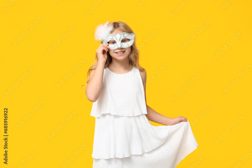 Adorable little girl wearing carnival mask on yellow background