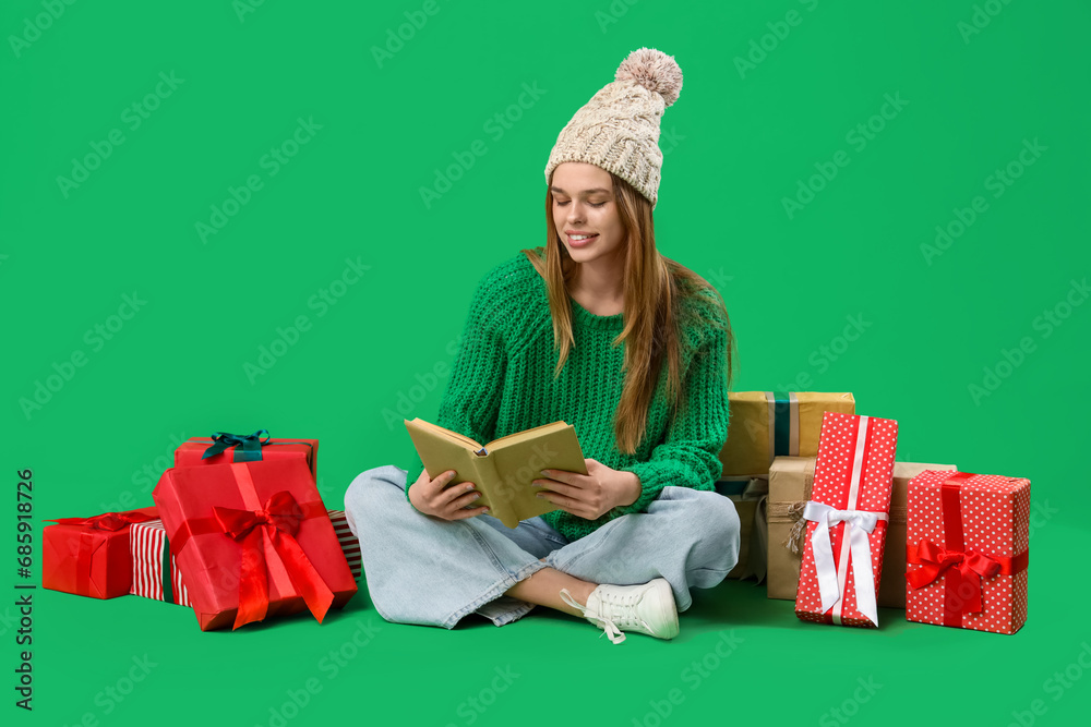Happy young woman with Christmas presents reading book on green background