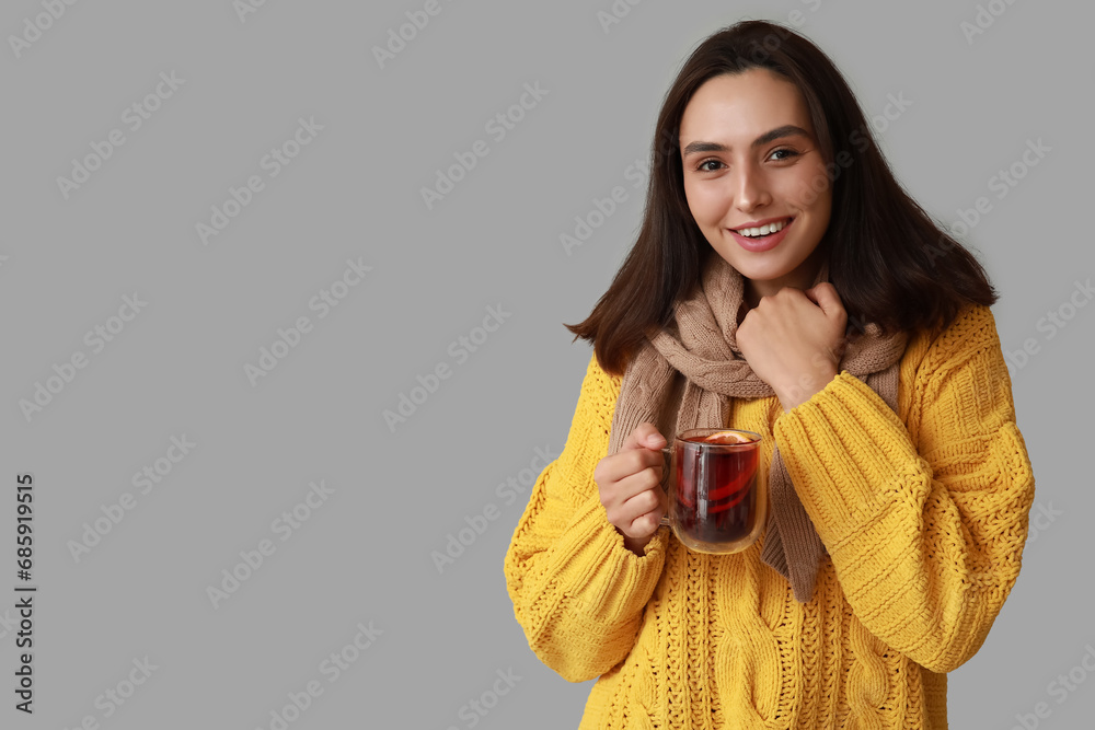Beautiful young woman in scarf with glass cup of hot mulled wine on grey background Beautiful young woman in scarf with glass cup of hot mulled wine on grey background