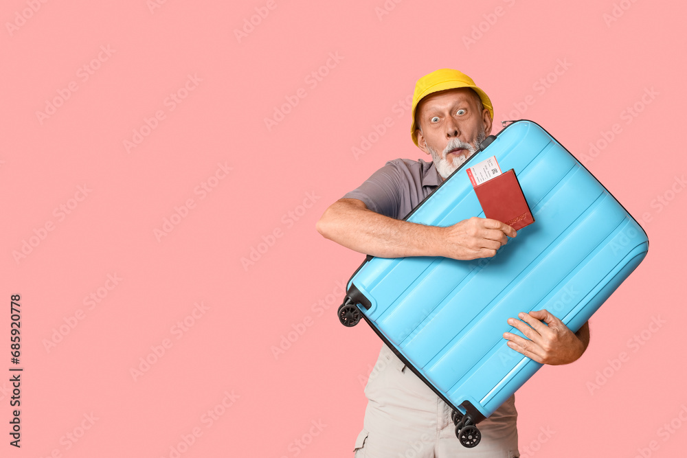 Surprised mature man with passport and suitcase on pink background. Travel concept Surprised mature man with passport and suitcase on pink background. Travel concept
