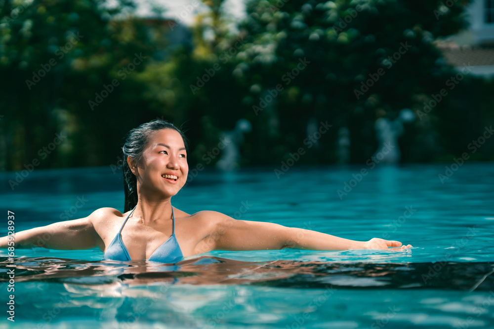 Young asian woman relaxing in the water, Beautiful girl relaxing at overwater infinity pool luxury resort. Spa, wellness, swimming.